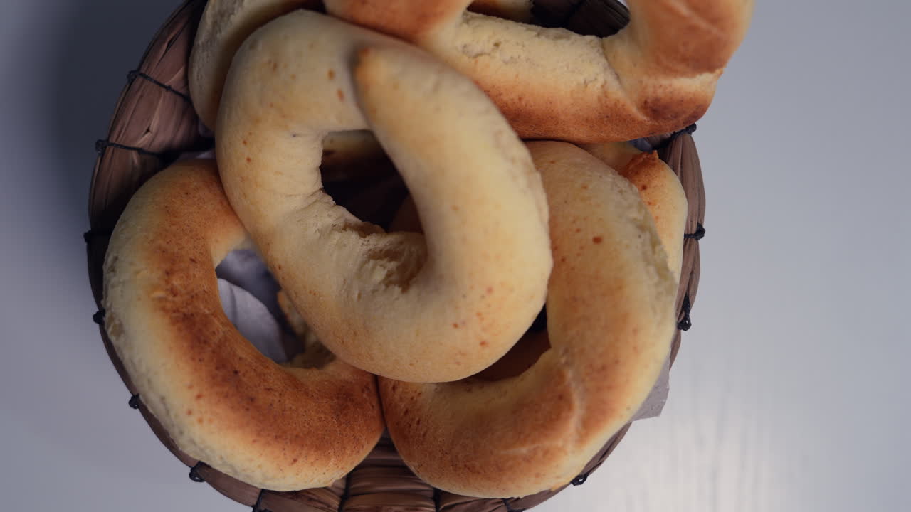 Savor the crisp texture of fresh pandebonos in a woven basket, top view. Warm tones and soft lighting highlight the Colombian pastry's artisanal quality