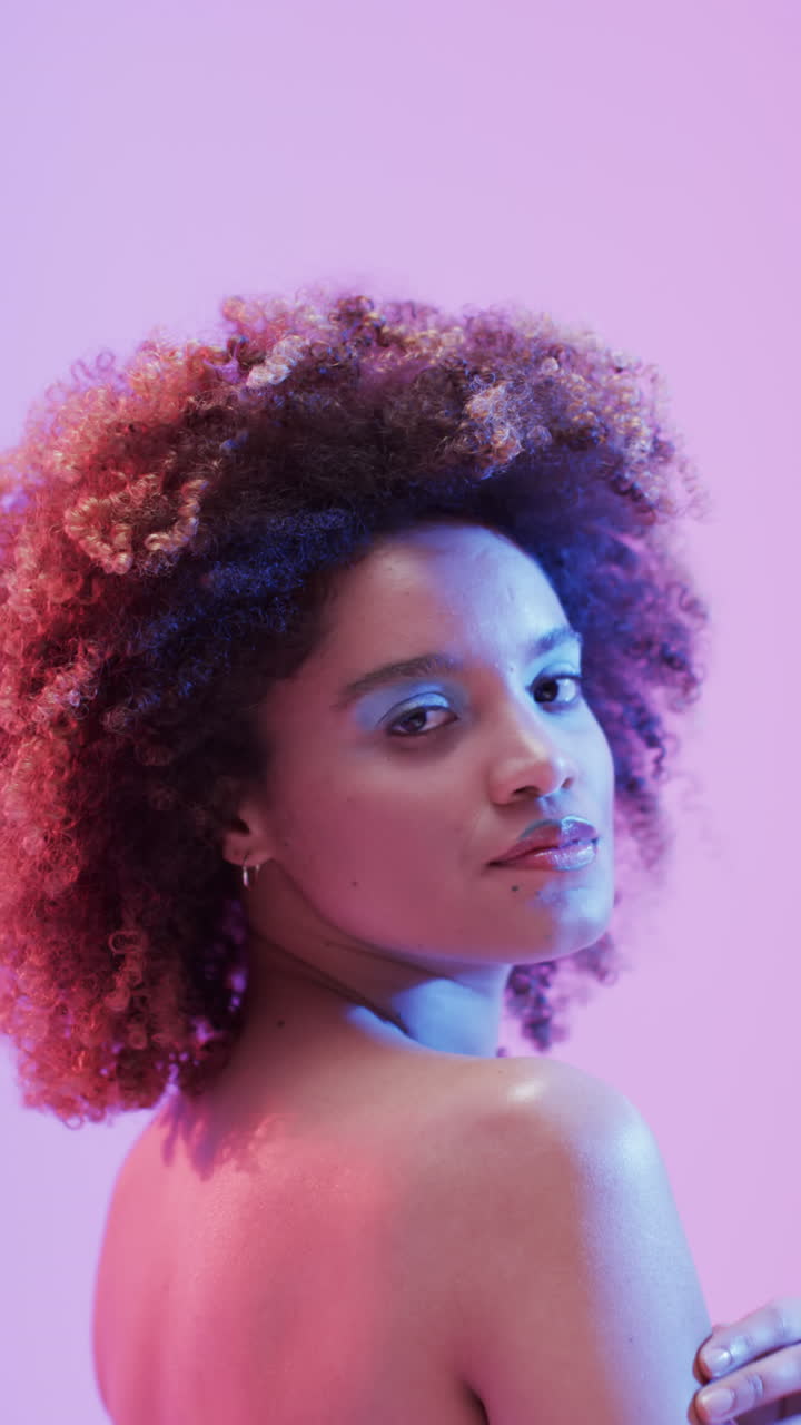 Vertical video of biracial woman with dark hair in blue and pink light, slow motion