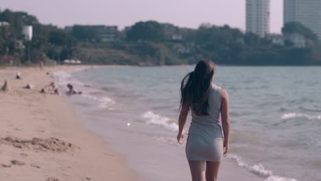 long haired lady in summer dress walks on sandy beach edge