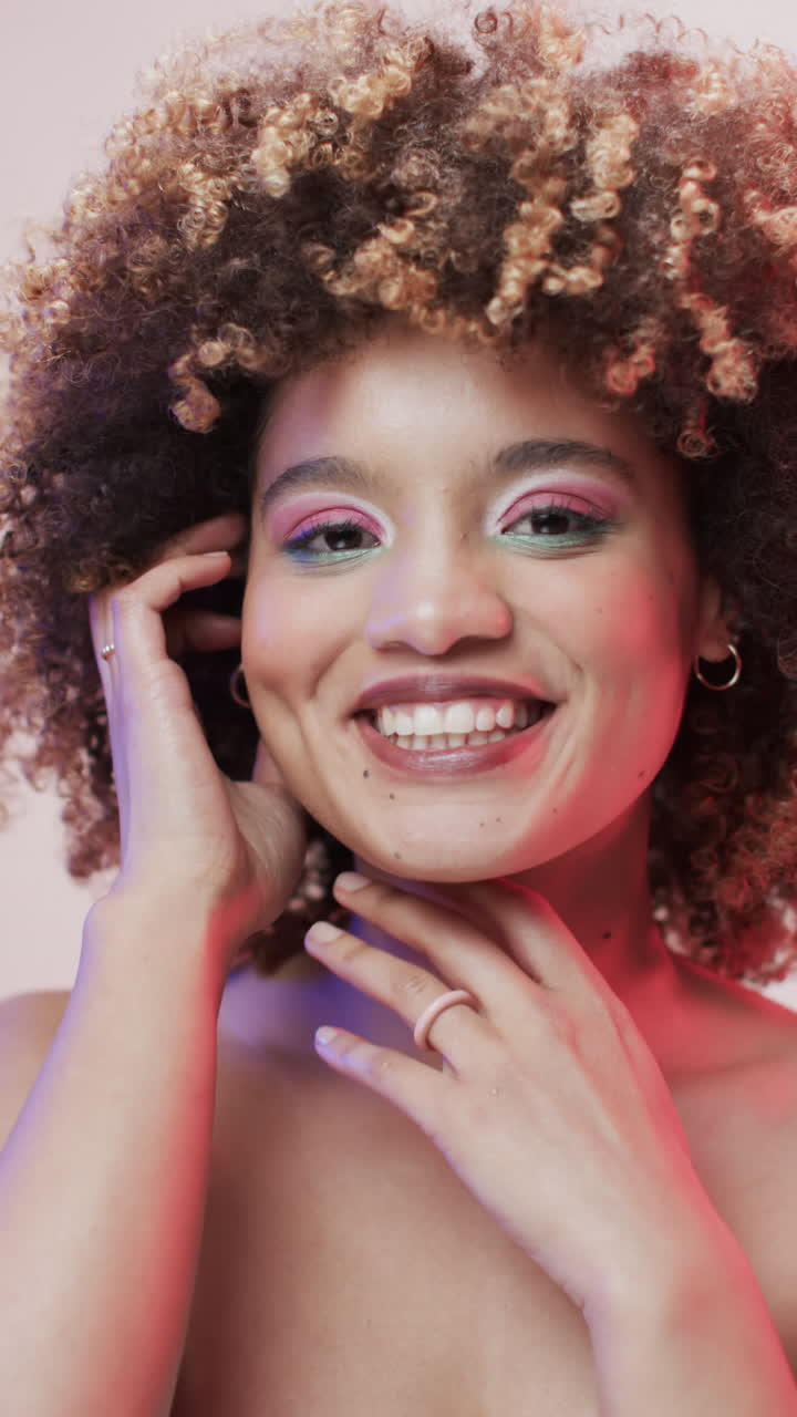 Vídeo vertical de mulher birracial feliz com cabelo escuro em luz azul e rosa, em câmera lenta.