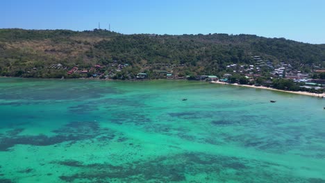 Türkisfarbenes-Wasser-Plätschert-Sanft-An-Die-Küste-Einer-Tropischen-Insel,-Mit-Booten,-Die-Die-Meereslandschaft-Und-Die-üppigen-Grünen-Hügel-Säumen