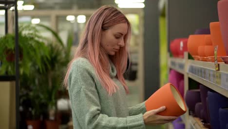 woman choosing clay pot for home plants from shelves of a flower shop