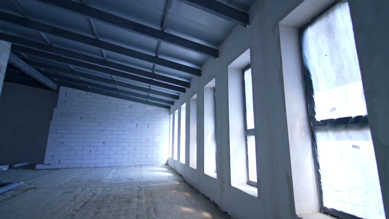 Large room with multiple big long windows. White brick walls and new roof in the building.