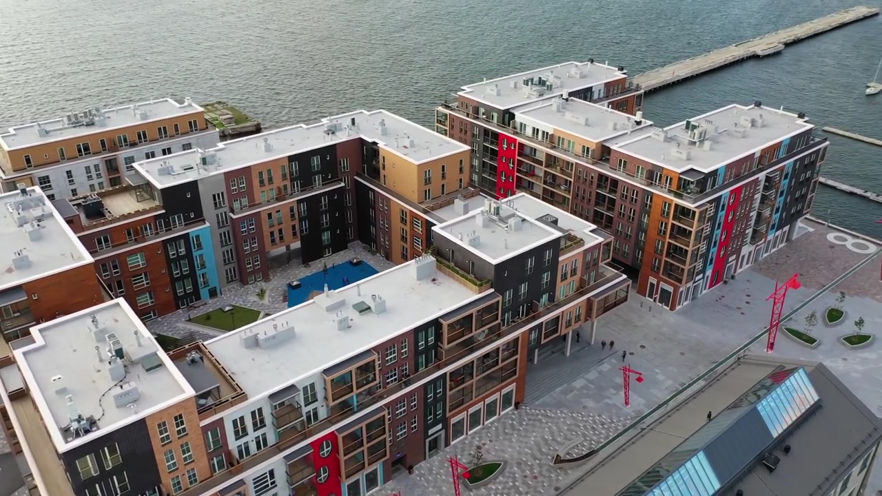 Vista aerea del quartiere Noblessner a Tallinn. L'inquadratura mostra cantieri navali storici in pietra convertiti accanto ad appartamenti di lusso moderni e lampioni di design rossi vicino al porto del Mar Baltico