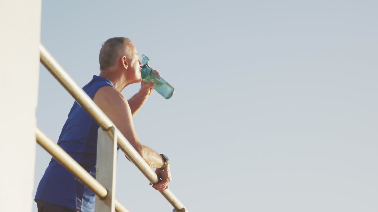 hombre mayor bebiendo agua en el paseo marítimo