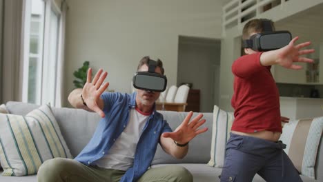 Kaukasischer-Vater-Mit-Sohn,-Der-VR-Headsets-Benutzt-Und-Im-Wohnzimmer-Sitzt