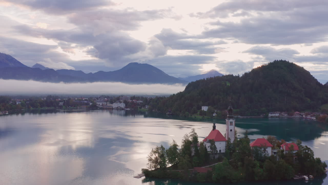 Ripresa aerea ascendente di una piccola chiesa su un'isola al centro del Lago di Bled, Slovenia.