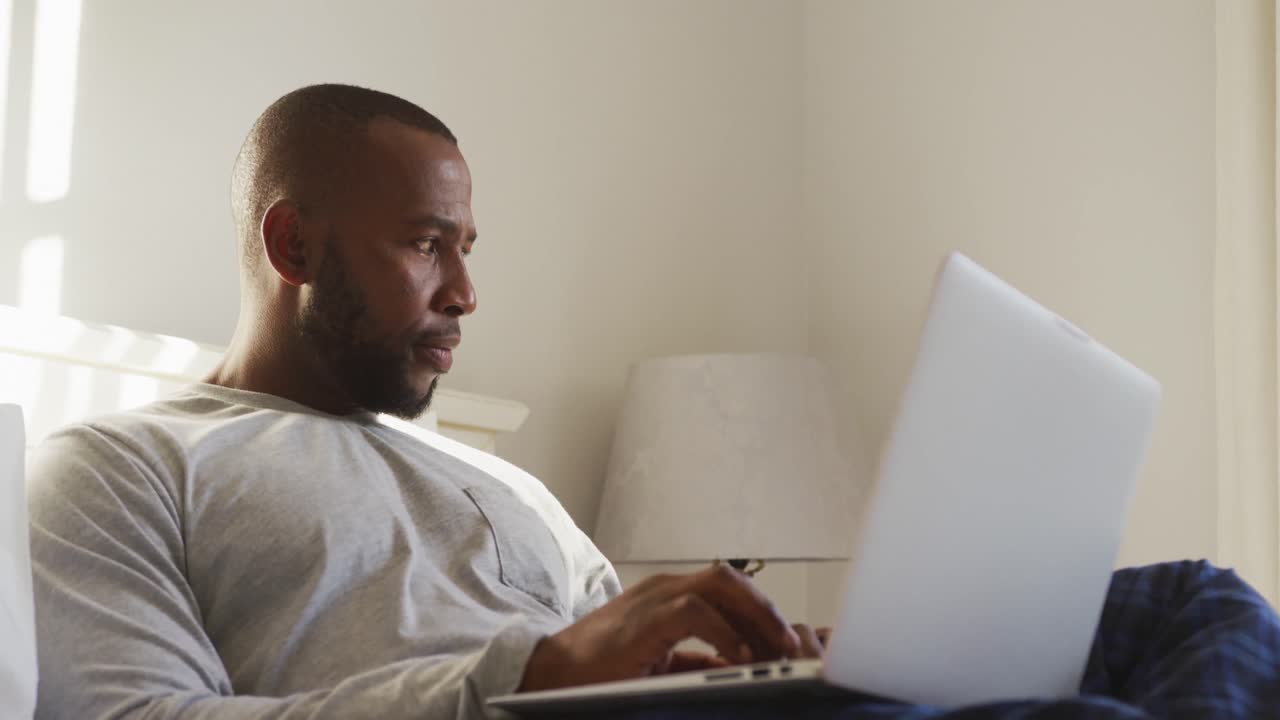 African american man using laptop while sitting on the bed at home