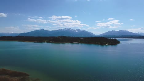 scenic 4k aerial view upon bavaria's famous lake chiemsee with its castle island herrenchiemsee and a ferry in the rural countryside with a beautiful blue sky and the alps mountains in the background