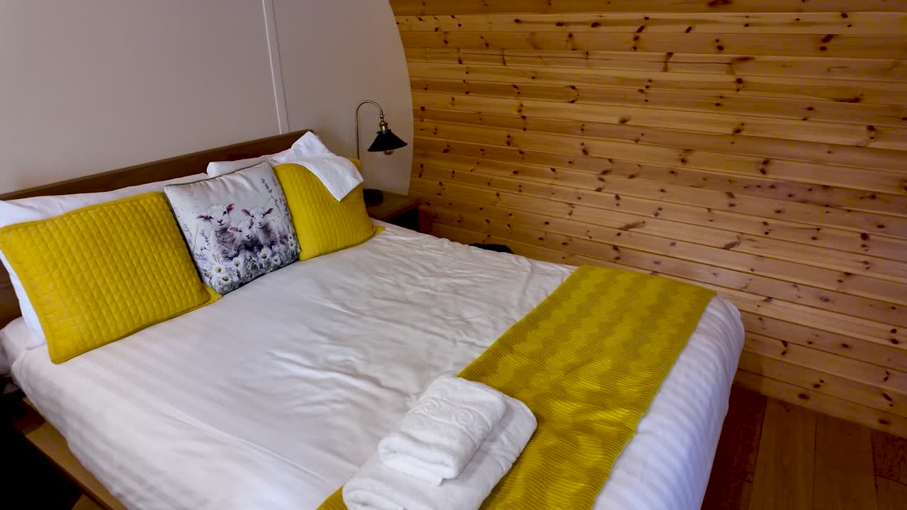 Warm, cosy bedroom in a wood cabin featuring a yellow-accented bed, white linens and folded towels