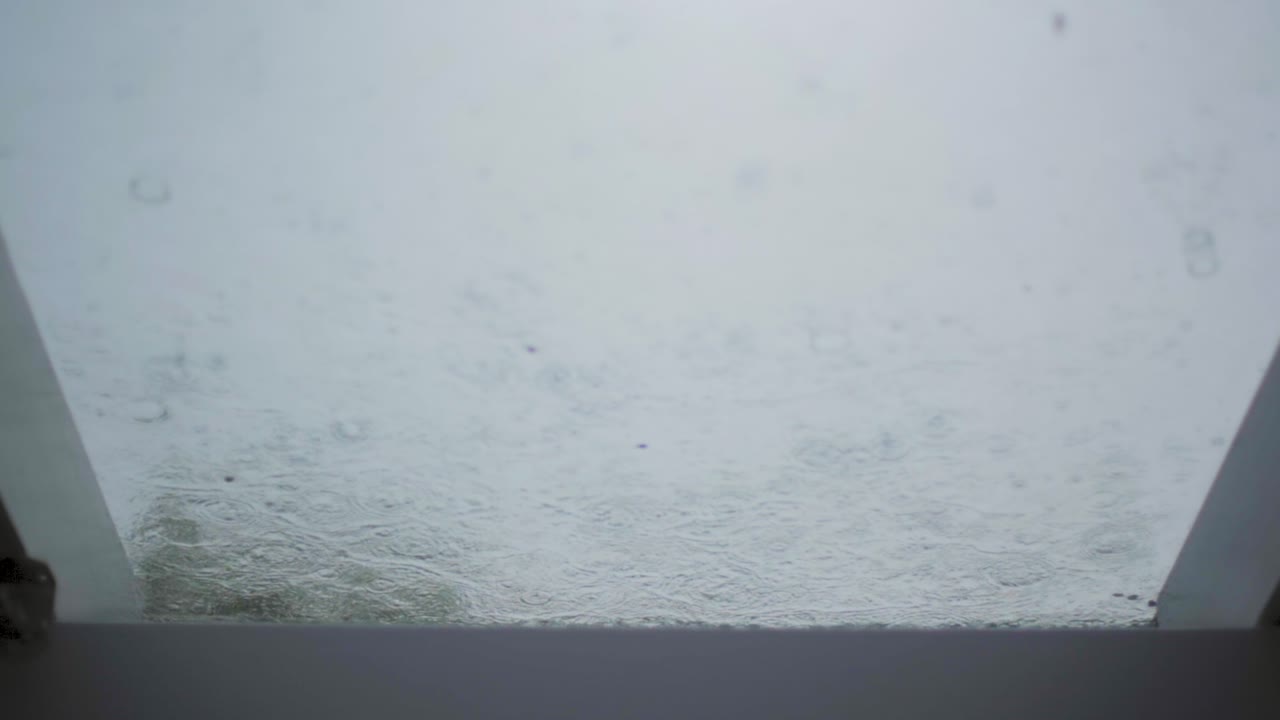 Slow motion: Rain drops falling on a glass roof. Camera panning with a slight focus pull