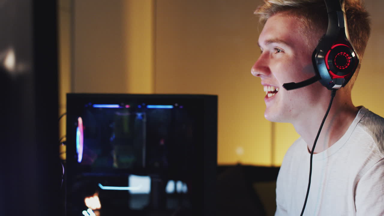 Excited Teenage Boy Wearing Headset Winning At Gaming At Home Using Dual Computer Screens