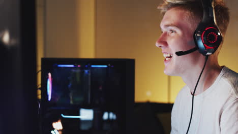 excited teenage boy wearing headset winning at gaming at home using dual computer screens