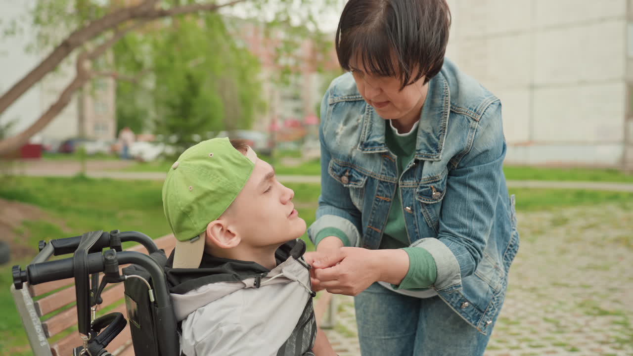 Gentle Aid On Park Pathway, Compassionate Care Connecting Caregiver And Young Man Outdoors, An Intimate Moment Of Trustful Support Between Caregiver And Young Man In Leafy City Park