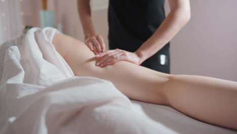 massage therapist gently squeezing client thigh with four fingers during relaxing wellness session, showing precise hand movement and therapeutic pressure in calm indoor setting with soft lighting