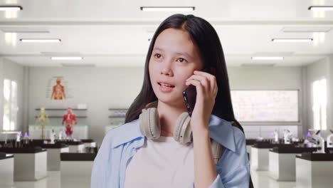 close up of asian teen girl student with a backpack talking on smartphone while standing in science laboratory