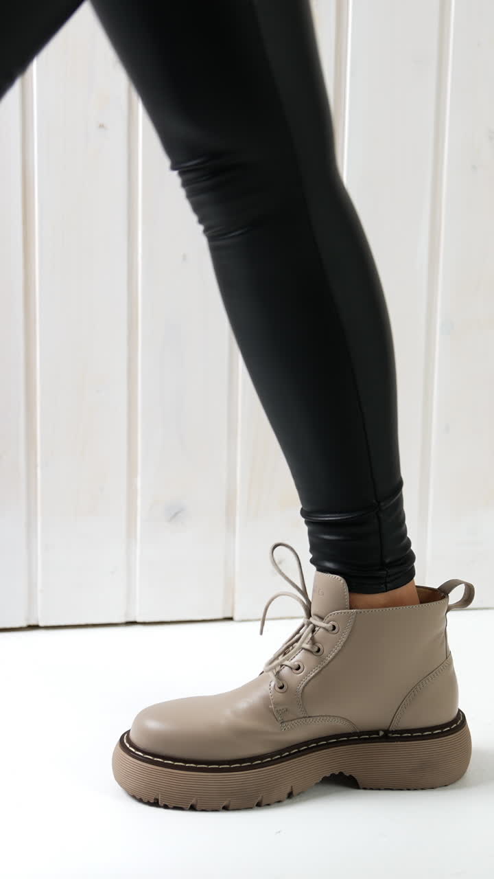 Model posing in beige boots on tractor soles. Woman wearing black leather leggings demonstrating stylish footwear. Vertical video