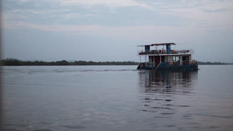 Große-Hausbootfähre-Fährt-In-Der-Abenddämmerung-Langsam-Durch-Den-Fluss,-Zeitlupe