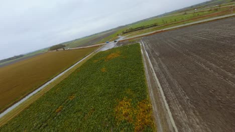 Drone-flying-over-a-plowed-field-going-towards-a-car-on-a-small-road