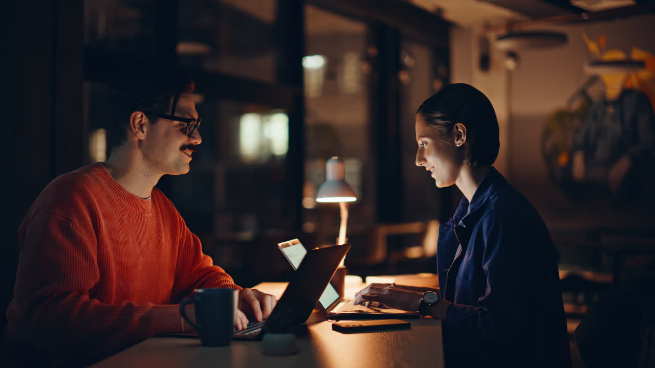 Smiling colleagues working overtime in dark office coworking space closeup