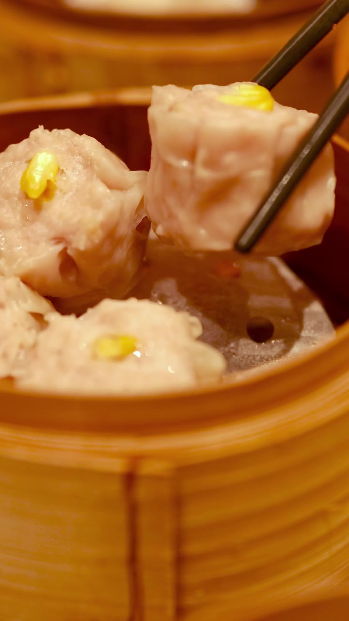 Sumpit mengangkat dim sum dari kukusan bambu dalam pencahayaan hangat, menonjolkan masakan tradisional Tiongkok di suasana restoran.