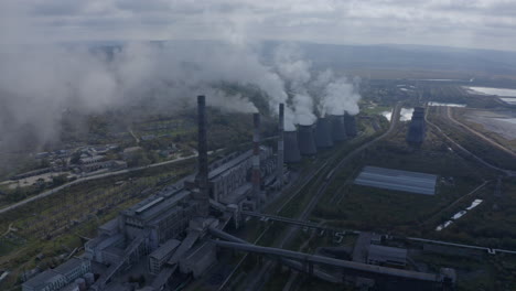 Slow-pivot-shot-of-a-coal-fired-power-station-with-its-chimneys-and-funnels-releasing-white-and-grey-smoke-into-the-air-on-a-sunny-and-cloudy-day