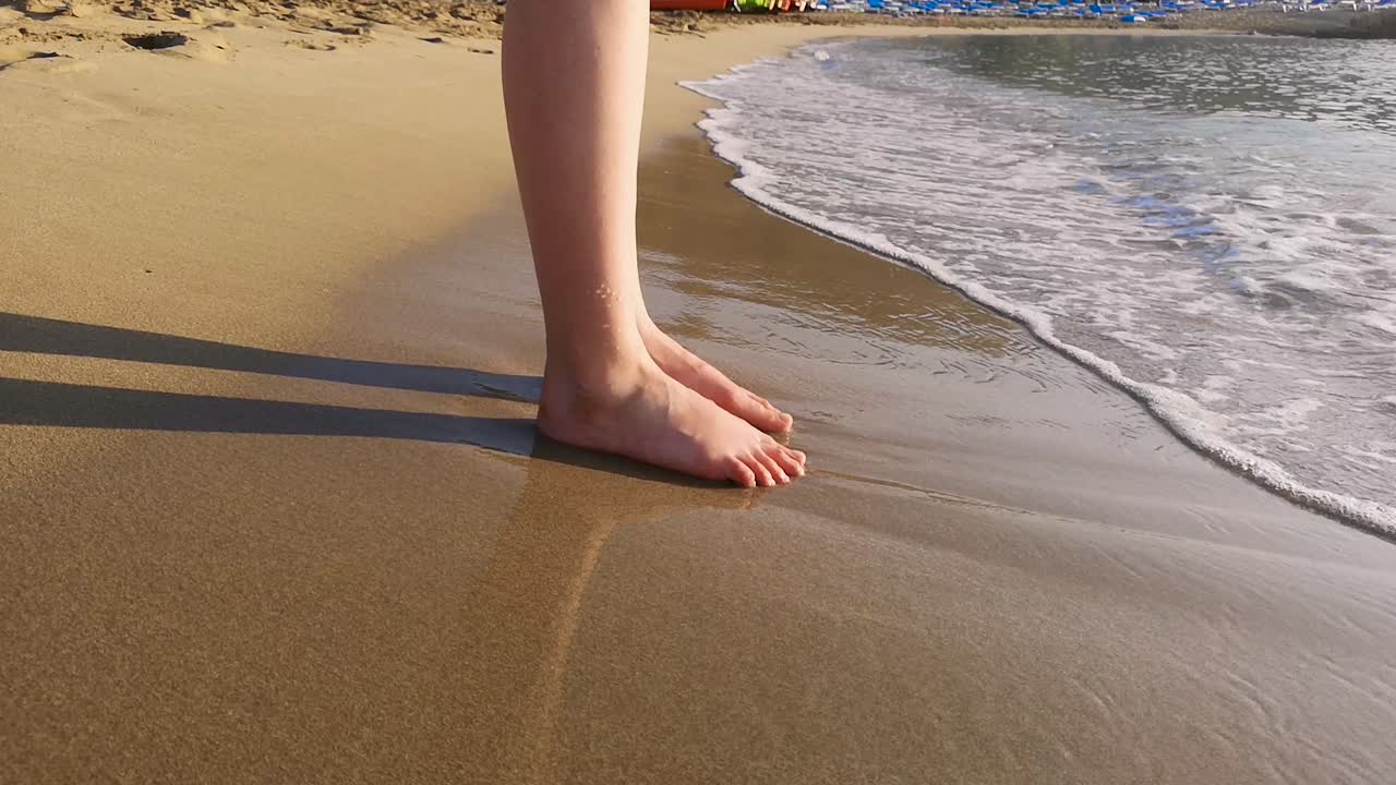 una mujer se para en la arena con los dedos de los pies en la arena y olas en la playa