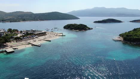 vista de drones en albania volando sobre playas de arena blanca, agua azul cristalina, pequeñas islas verdes, barcos y hoteles, día soleado en ksamil