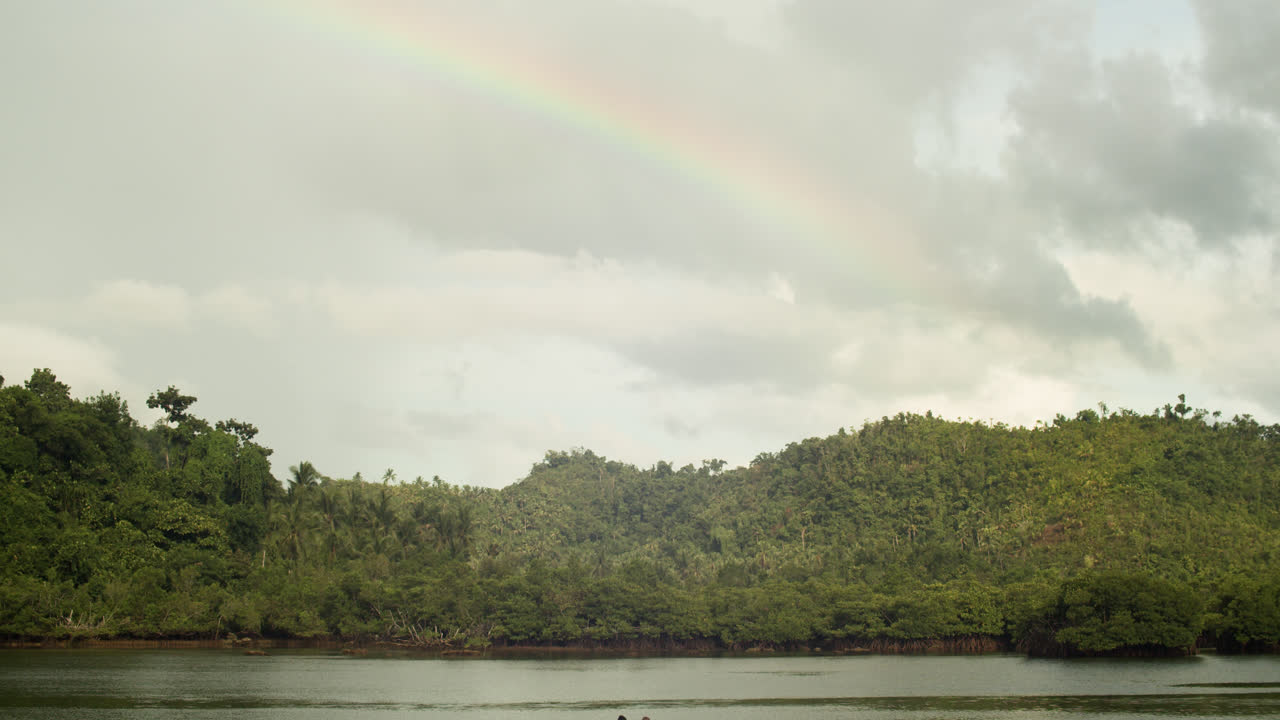 Time-laps of a cloudy day on a mangrove forest and a backdrop of a rainbow in Secret Beach, Siargao.