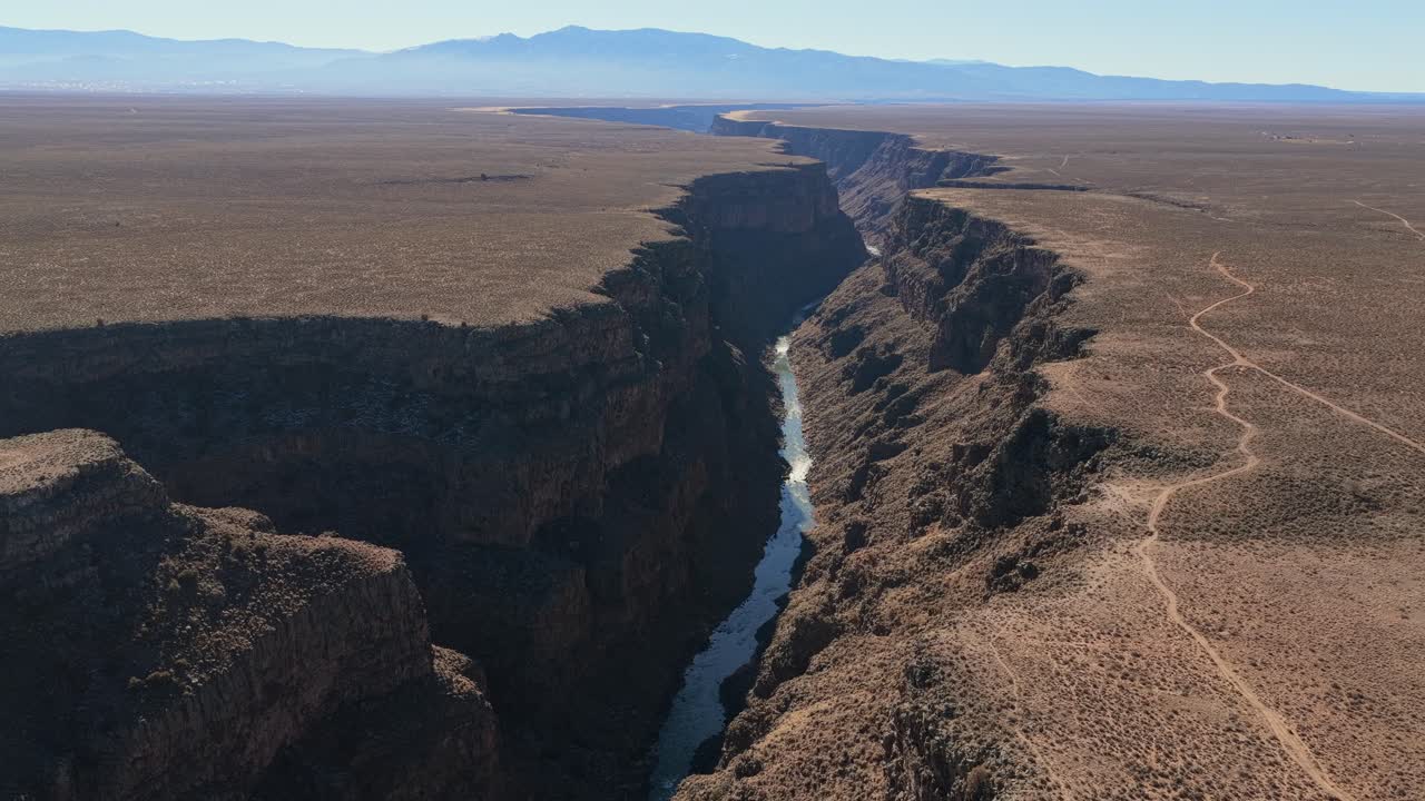 Expansive, cinematic horizon view of the entire winding river canyon system. The Rio Grande River cuts dramatically across the massive high desert plateau of the American Southwest