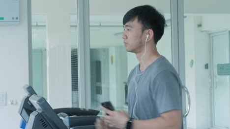 young asian man running on the treadmill in the gym with earphones