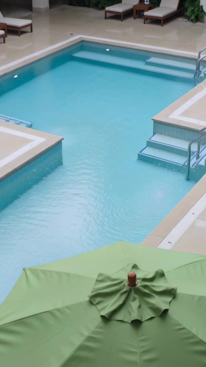 Vertikal video: Kamera panorerer ned fra terrasse, viser rydning af blade og en turkis pool.