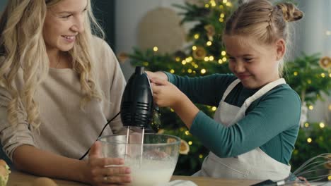 caucasian mother and daughter preparing baking using electric mixer in the kitchen before christmas.