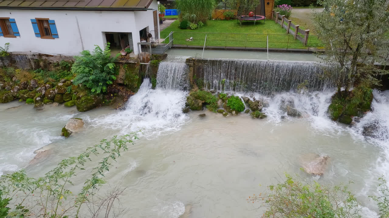 Pan across water spilling over dam into river in Bavarian foothills