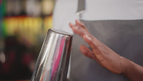 black barman taps shining shaker bottom in bar closeup. african american barkeeper shakes out cocktail drops from cup in nightclub. man prepares beverage