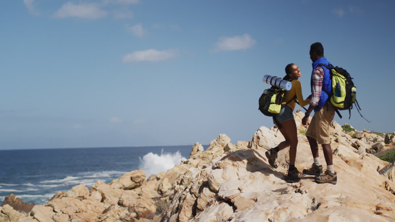 pareja afroamericana subiendo a las rocas mientras hacen trekking
