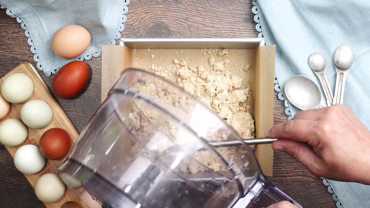 Pressing in the pastry crust into a square baking pan to make pecan caramel brownies. Making a dessert with a pastry crust on the bottom. Pie or cookie crust being pressed into a baking pan.