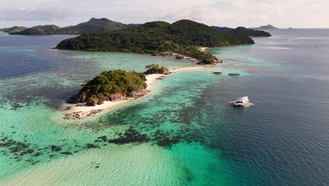 aerial drone view of coron island’s dramatic cliffs, tropical greenery, and idyllic turquoise waters, philippines. descending shot towards small islands and boats in the water.