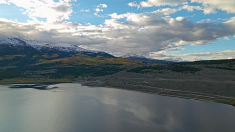 aerial footage of a vast lake surrounded by green hills and snow-capped peaks in the distance