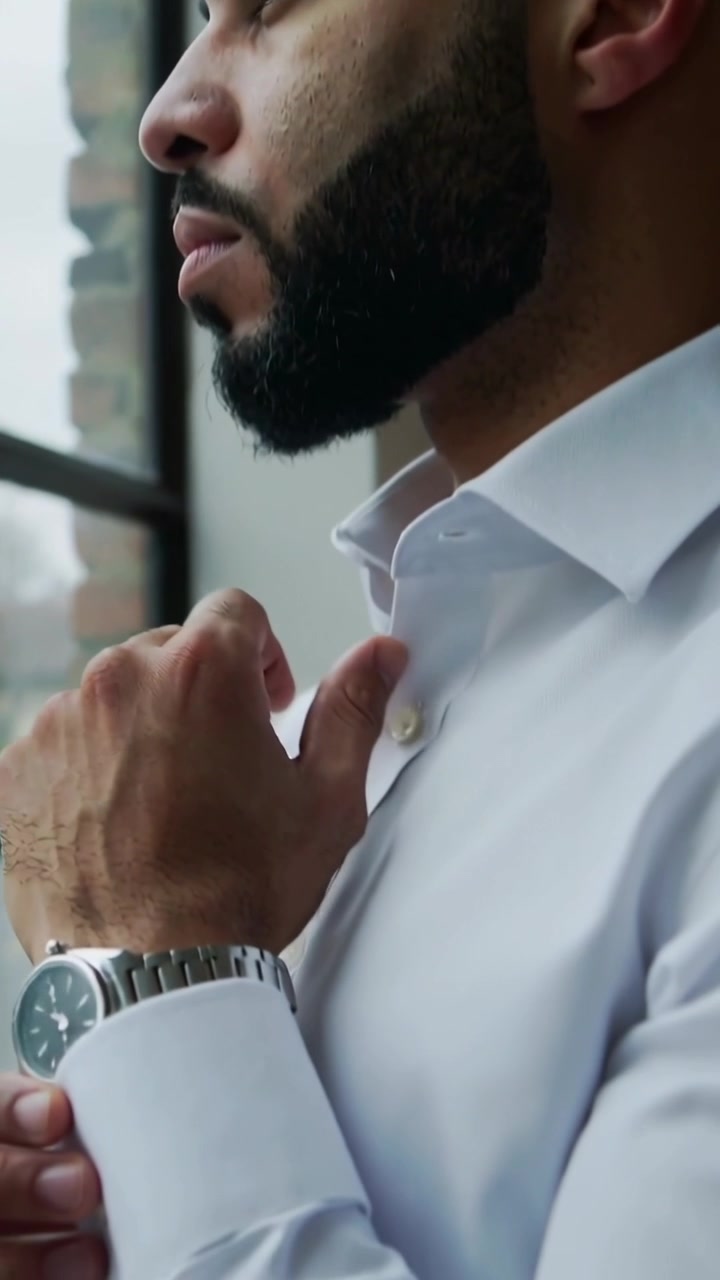 Video vertical: Mirando por la ventana, hombre con camisa blanca ajustándose el puño y el reloj, preparándose para el trabajo
