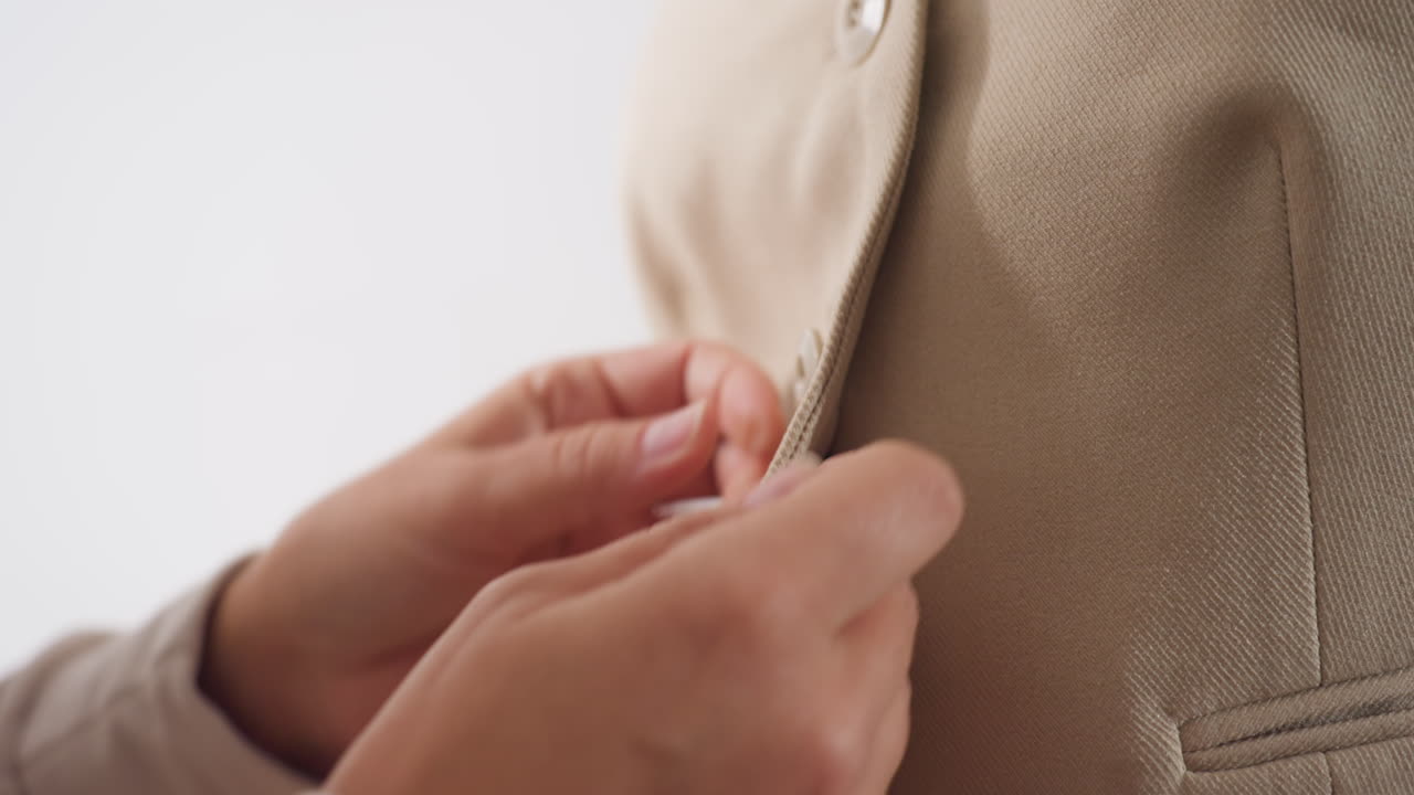 Hands of designer gently button up beige lapel blazer on mannequin, smoothing fabric, aligning edges, checking fit and drape, showcasing craftsmanship during focused tailoring session in workshop