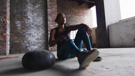 African-american-man-sitting-resting-after-exercising-with-medicine-ball-in-an-empty-urban-building