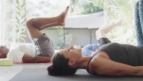 focused diverse seniors doing pilates, stretching on mats with female coach, unaltered, slow motion