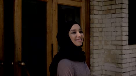 young happy muslim girl in hijab is coming out of university in daytime in summer, squinting, religious concept, studying concept