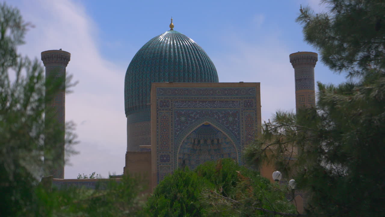 turquoise tiled dome and twin minarets seen through soft green foliage clear blue sky ornate Islamic mosaic facade calm heritage architecture mood Timeless heritage mood suitable for culture