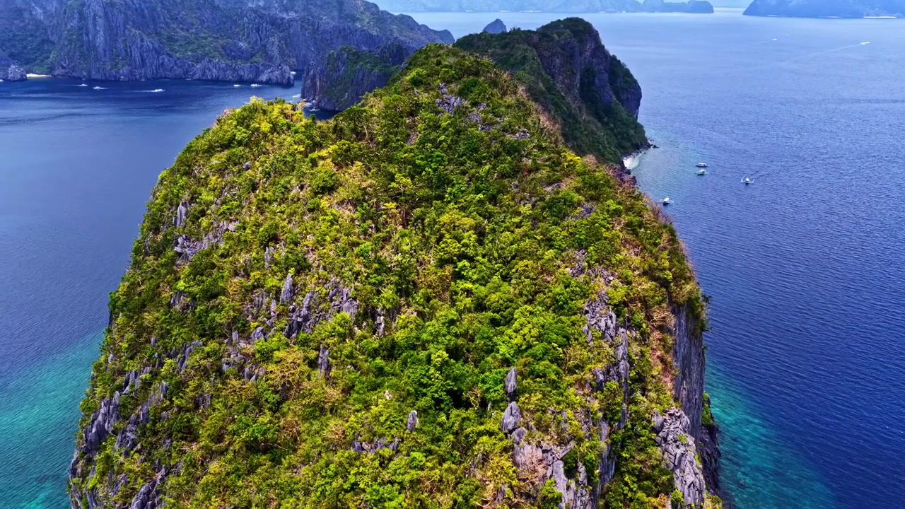Spettacolare ripresa con drone su El Nido, Palawan, Filippine. Mostra un'enorme isola di scogliera calcarea che emerge dalle profonde acque blu dell'oceano accanto a una tradizionale barca a bilanciere in una giornata limpida.