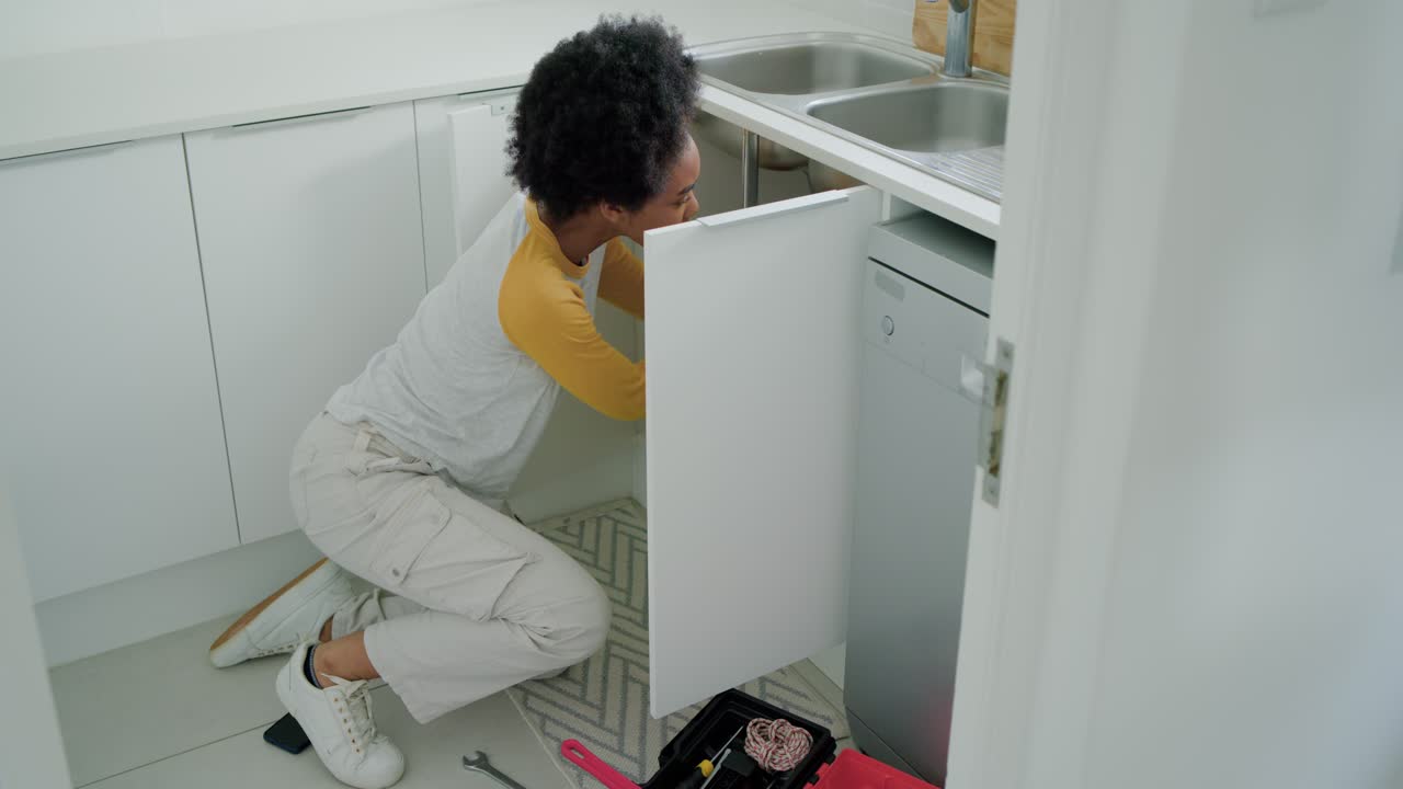 African woman picking tools from red toolbox kneeling in kitchen testing faucet confirming fix