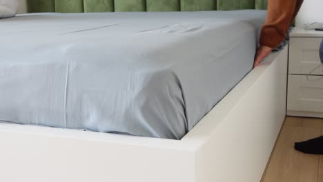 a person making a bed with white sheets and a gray bedspread