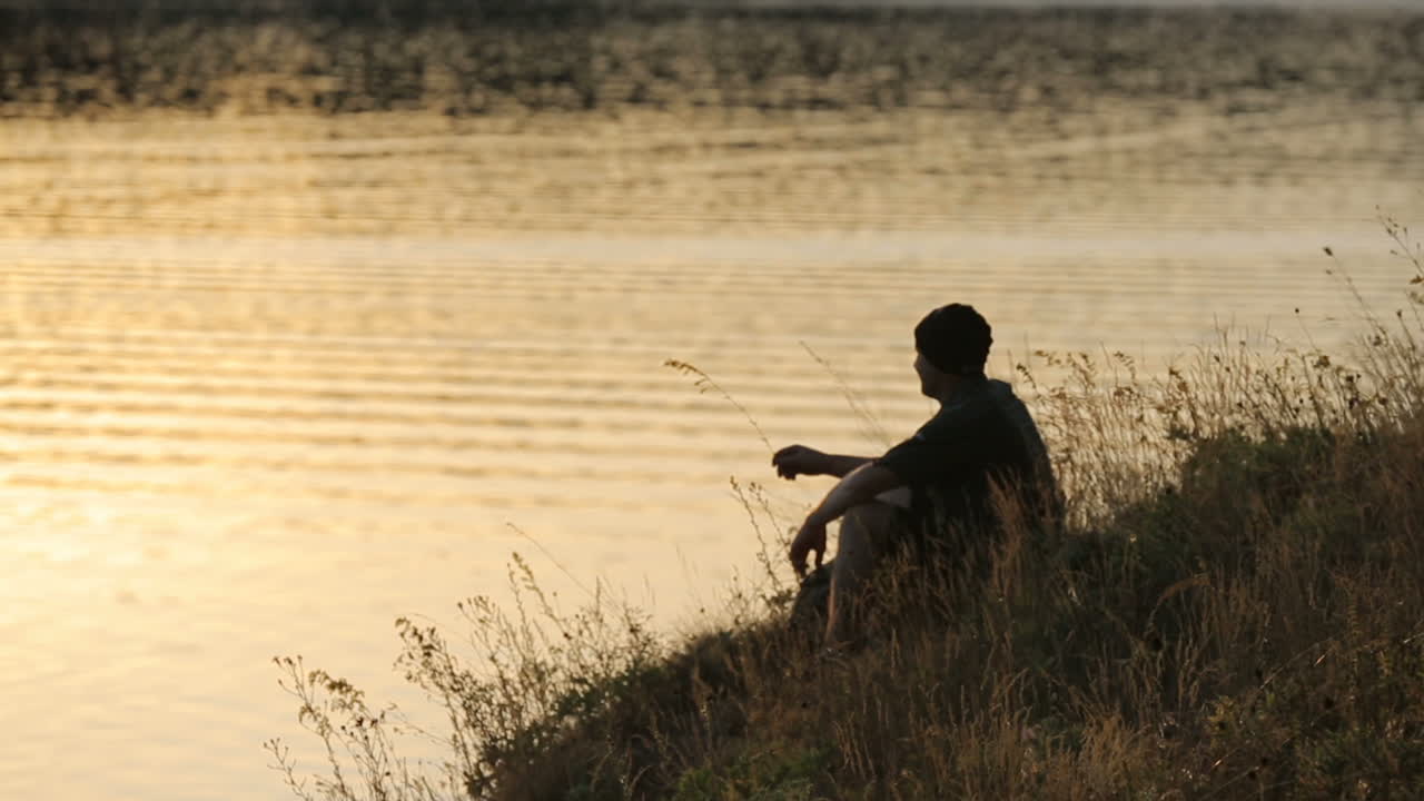 Tourist With Backpack Sitting On A Hill. Adult man tourist with backpack sitting on a hill and enjoying evening landscape