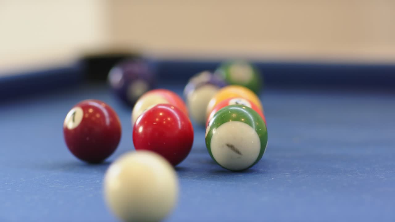 Cue striking cue ball initiating break shot on pool table balls shattering spreading toward pockets